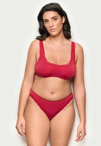 Sujetador rojo y braguitas a juego hechas de una tela suave, con un borde de encaje a lo largo de los bordes y tirantes, que muestran un diseño sin costuras.