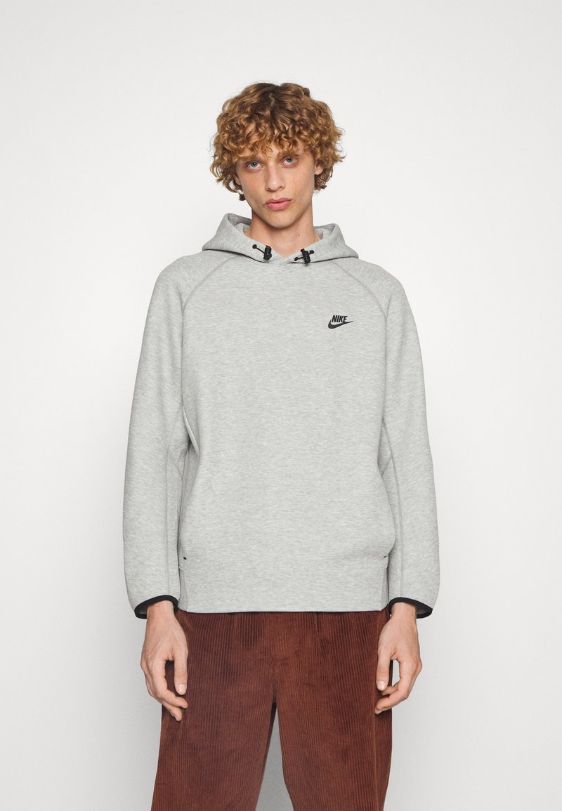 Sweat-shirt à capuche gris avec une texture douce, arborant un logo Nike noir sur la poitrine et des accents noirs contrastants sur les poignets.