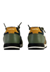 Zelené a námořnické běžecké boty s žlutými akcenty, gumovými podešvami a poutky. Vlastnosti zahrnují logo na zadní straně a kontrastní bílou mezipodešev.