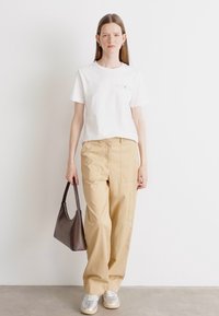 Maglietta bianca, pantaloni beige larghi, sneakers grigie e una borsa grigia scura. Design semplice, modelli minimalisti e texture morbide.