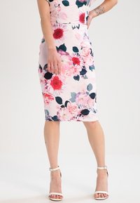 Vestido de lápiz floral con fondo rosa, que presenta grandes flores rojas y rosas y hojas verde oscuro. Tejido suave y diseño hasta la rodilla.