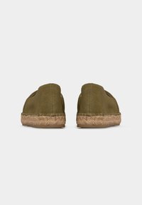 Paire de chaussures olive à enfiler avec semelles en jute tissé, vues de dos sur un fond clair uni.