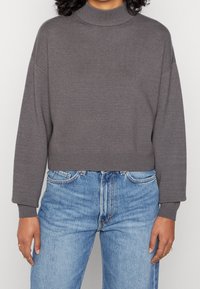Pull gris court avec un col haut, des poignets et un ourlet côtelés. Associé à un jean en denim bleu clair avec un design classique à cinq poches.