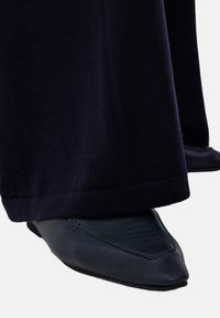 Zwarte leren puntneus schoen met een gladde textuur, gecombineerd met donkere stoffen broek, wat zorgt voor een nette en op maat gemaakte uitstraling.