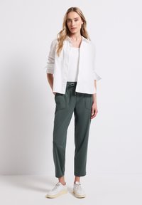 Biała koszula zapinana na guziki, zielone spodnie z kieszeniami i białe sneakersy. Koszula ma podwinięte rękawy; spodnie są zwężane i mają elastyczny pas.