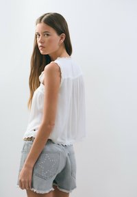 Blusa sin mangas blanca con borde de encaje, combinada con shorts de mezclilla gris claro que presentan recortes en forma de estrella y bordes deshilachados.