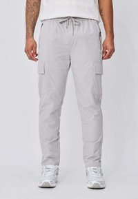 Pantalon cargo gris clair avec taille à cordon et poches latérales, porté avec des baskets blanches.