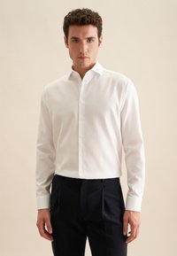 Witte langärmige shirt met een button-down kraag, met een subtiele textuur. Gecombineerd met donkere broeken, heeft het een passend en gestroomlijnd silhouet.