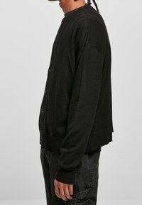 Czarny kardigan, dzianinowy materiał, zapięcie na guziki, okrągły dekolt, długie rękawy, ściągacze na mankietach i u dołu, luźny krój, brak widocznych wzorów.