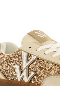 Zapatillas con una parte superior de cuero beige, acentos de purpurina dorada, logo blanco y cordones. Cuenta con una suela de goma texturizada en tono marrón.