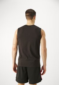 Černé bezrukávové tričko z bavlny s klasickým kulatým výstřihem, nošené s tmavými sportovními šortkami z jemné síťoviny s červenými akcenty.