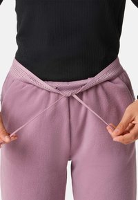 Purple fleece joggers with a textured waistband and drawstring, held by hands, showcasing the garment's softness and fit.