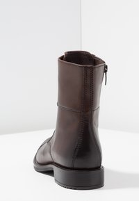 Botín de cuero marrón hasta el tobillo con textura suave, cremallera lateral y detalles de costura. El tacón es sólido, proporcionando estabilidad y comodidad.