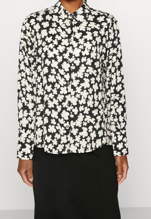 Czarna koszula zapinana na guziki z białym abstrakcyjnym kwiatowym wzorem, noszona z prostą czarną spódnicą, widoczna od ramion do bioder.