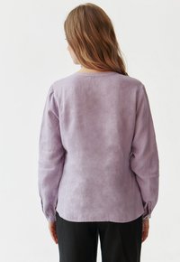 Lavender langekragen shirt met een relaxte fit, ronde halslijn en knoopmanchetten. De stof heeft een gestructureerde afwerking; de achterkant is licht gebogen.