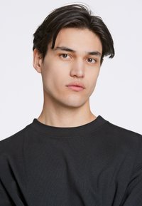 La camiseta negra de cuello redondo presenta una textura suave y un ajuste relajado, con un diseño sencillo, costuras mínimas y sin logotipos visibles.