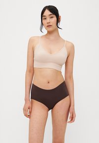 Beige ribbed bralette dengan tali tipis dipadukan dengan celana dalam cokelat berpinggang tinggi. Tekstur halus dan desain sederhana, menekankan fungsionalitas.