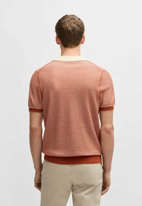 Kortärmad polo skjorta i ljus orange med texturerad stickning. Har en kontrasterande krämfärgad krage och ribbade ärmslut och nederkant. Skräddarsydd passform.