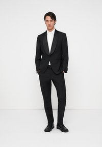 Svart tuxedo med satinrevers, skräddarsydd passform och smala byxor. I kombination med en vit skjorta och svarta fin skor. Slät tygtextur.