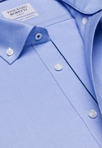 Camicia di cotone azzurro chiaro con un motivo testurizzato, colletto button-down e bottoni bianchi. Presenta un'etichetta per "Vincenzo Boretti." Design aderente.
