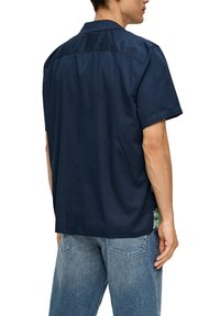 Marineblauwe kortekousen shirt van katoen, met een kraag en een rugventilatie. Het ontwerp omvat een gemusterde zijpaneel met tropische bladeren.