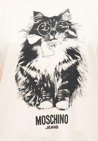 Αφράτη γάτα που φορά στρογγυλά γυαλιά και έχει ένα φιόγκο στο στόμα της, με το κείμενο «MOSCHINO JEANS» κάτω από την εικόνα.