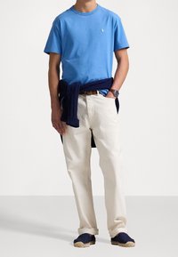 Camiseta de algodón azul claro con un logo, pantalones de algodón color crema y alpargatas navy. Un suéter navy está atado a la cintura.