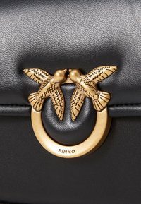 Black leather bag featuring a textured surface and a gold-tone hardware closure shaped like two birds facing each other.