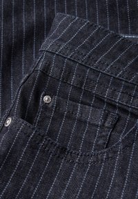 Tmavě modrá denimová látka s modrými pruhy, obsahující detail kapsy a stříbrné cvoky. Textura je hladká s jemným leskem.