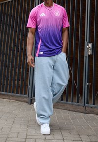 Adidas jersey features a gradient of pink to purple with triangular patterns, paired with loose light blue denim pants and white sneakers.