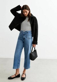 Zwarte wolmix cropped jasje, gestreepte slim-fit top, hoogstaande blauwe spijkerbroek met wijde pijpen, zwarte ballerina's en een kleine zwarte handtas.