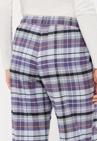 Pantalons de pyjama à carreaux violets avec une taille élastique, comprenant des accents bleus, noirs et oranges dans un tissu doux et texturé. Vue arrière affichée.