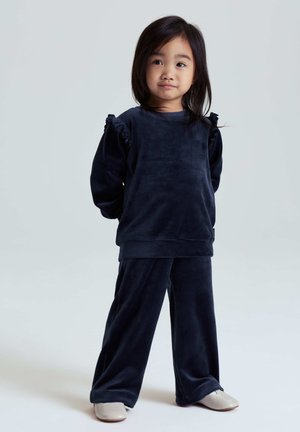 Marineblauw velours trainingspak met lange mouwen met ruches en losse broekspijpen. Gladde textuur, eenvoudig ontwerp en neutraal schoeisel.