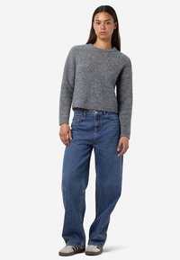 Γκρι πλεκτό πουλόβερ με στρογγυλή λαιμόκοψη, συνδυασμένο με φαρδιά μπλε τζιν τζιν και γκρι αθλητικά παπούτσια. Σχεδιασμός άνετης εφαρμογής και υφή υφάσματος.