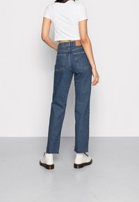 Högmidjade blå denim jeans med rak bendesign, två bakfickor och stickade detaljer; kombinerat med en enkel vit croppad topp.