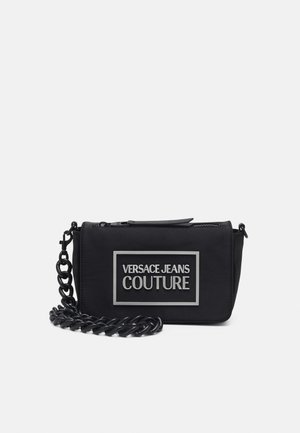 Czarna torebka na ramię Versace Jeans Couture z prostokątną naszywką z logo i grubym łańcuszkowym paskiem na białym tle.