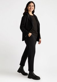 Blazer noir avec des revers en satin, haut noir et pantalon noir ajusté. Pour parfaire le look, des bottines noires avec une semelle texturée.