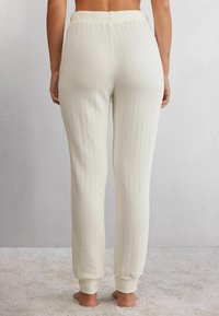 Crèmekleurige ribfluwelen broek met een elastische tailleband en strakke boorden. Zacht materiaal met verticale strepen, ontworpen voor een tapse pasvorm.