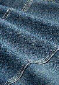 Tessuto di denim blu, caratterizzato da una superficie leggermente texture e cuciture visibili. Il materiale presenta un aspetto morbido e consumato con sottili variazioni.