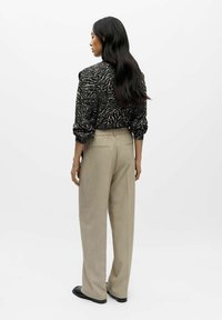 Sweter w czarno-kremowy wzór zebry z bufiastymi rękawami, w połączeniu z beżowymi spodniami o wysokim stanie. Modelka stoi tyłem do aparatu.