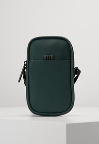 Zelená taška s měkkou strukturou a obdélníkovým tvarem, s přední kapsou, zipovým uzávěrem a ramenním popruhem. Minimalistický design.