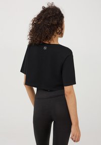 Maglietta nera a cropped in morbido cotone. Presenta maniche corte, un collo rotondo e un piccolo logo sul retro.