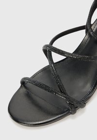 Sandale noire plate avec des lanières entrecroisées en matériau texturé. La semelle est lisse, mettant en avant un design minimaliste.