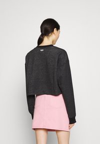 Beskuren svart sweatshirt med långa ärmar och ribbade mudd, tillsammans med en ljusrosa denimkjol med bakfickor.