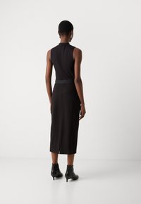 Haut sans manches noir avec un col montant, associé à une longue jupe noire avec une fente arrière, complété par des bottines noires.