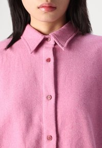 Pink wool shirt with a collar, featuring a placket of matching buttons and a soft, textured fabric.