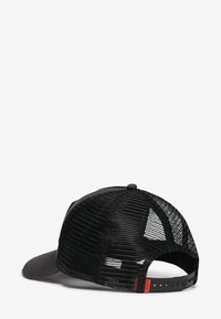 Gorra de camionero negra de malla con correa ajustable de cierre a presión y etiqueta roja pequeña en la parte trasera, mostrada desde un ángulo posterior.