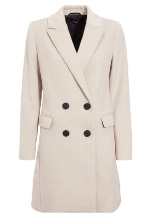 Cappotto doppiopetto beige con lapels affilati, bottoni neri, tasche laterali e un tessuto leggermente strutturato, caratterizzato da una vestibilità su misura.