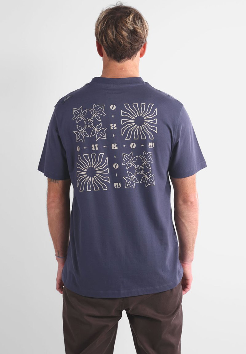 T-shirt en coton bleu marine avec un imprimé graphique au dos présentant des motifs floraux et des rayons de soleil en crème. Manches courtes et col ras du cou.