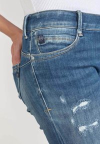 Světle modré džíny s úzkým střihem, se střiženými detaily, viditelným švem, zapínáním na knoflík a malým logem na přední kapse.